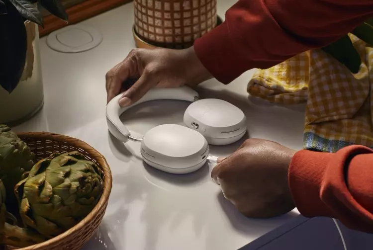 A fehér Sonos Ace fejhallgatót töltéshez csatlakoztató személy a konyhában
