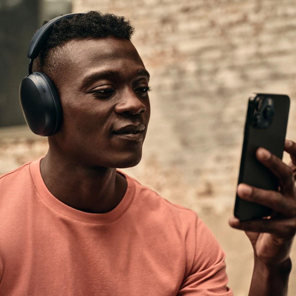 Férfi felhasználó a telefonnal, miközben egy fekete Sonos Ace fejhallgatóval hallgatja a zenét.