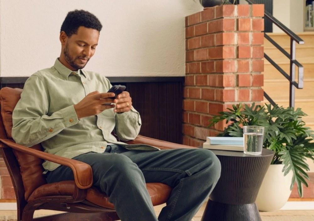 A Sonos App felhasználója a telefonon ül a nappaliban